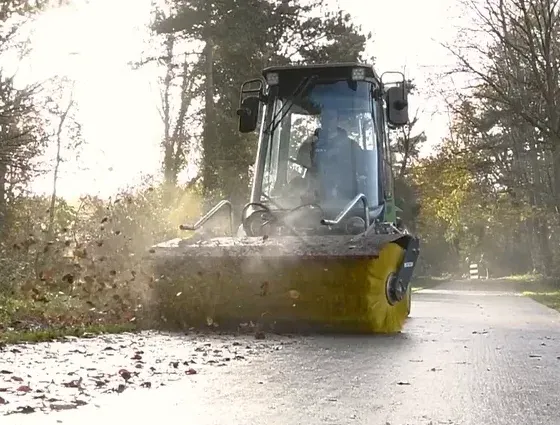 LM Trac with a sweeper attachment cleaning a pathway in a park.